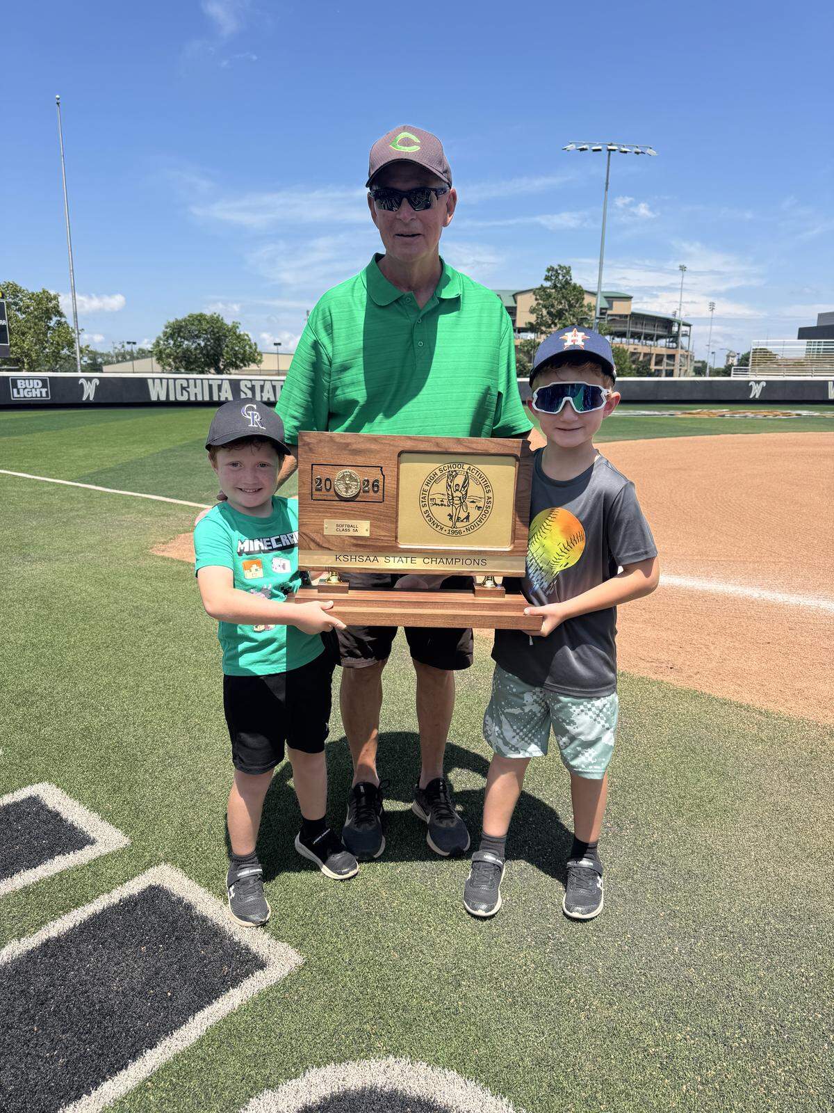 Bishop Carroll softball coach Steve Harshberger poses with his two grandchildren and the Class 5A championship trophy after the Golden Eagles beat St. Thomas Aquinas 3-2 on Saturday at Wilkins Stadium. Harshberger survived a near-death health scare last summer.