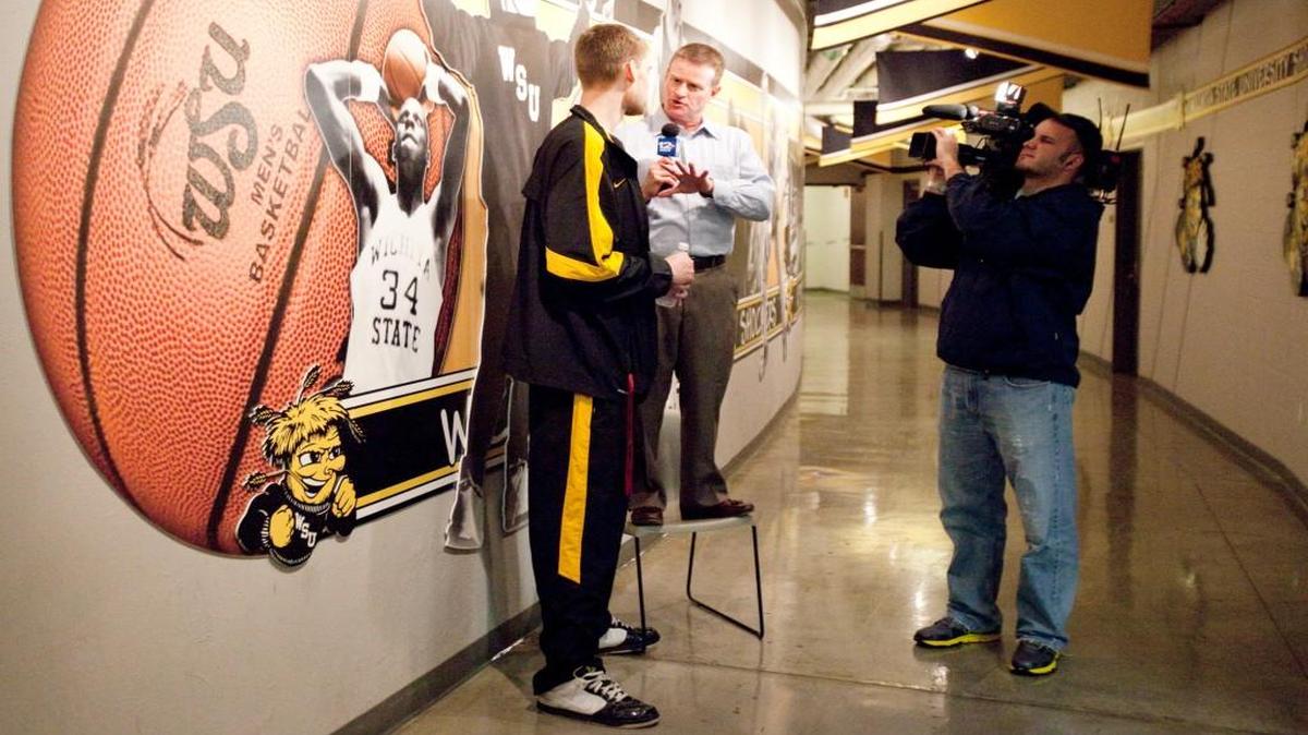 Bruce Haertl stands on a chair to interview 7-footer Garrett Stutz as Wichita State prepared for the 2011 postseason.