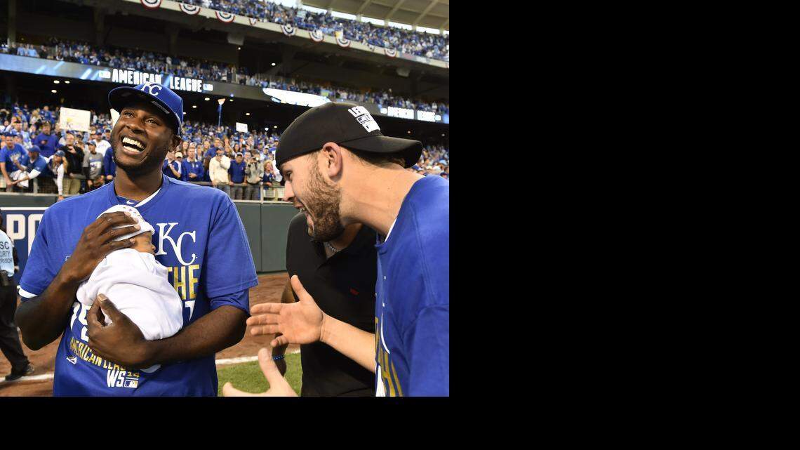 Kansas City Royals center fielder Lorenzo Cain holds his young son Cameron Loe Cain as teammate third baseman Mike Moustakas celebrate after Royals won the American League pennant.