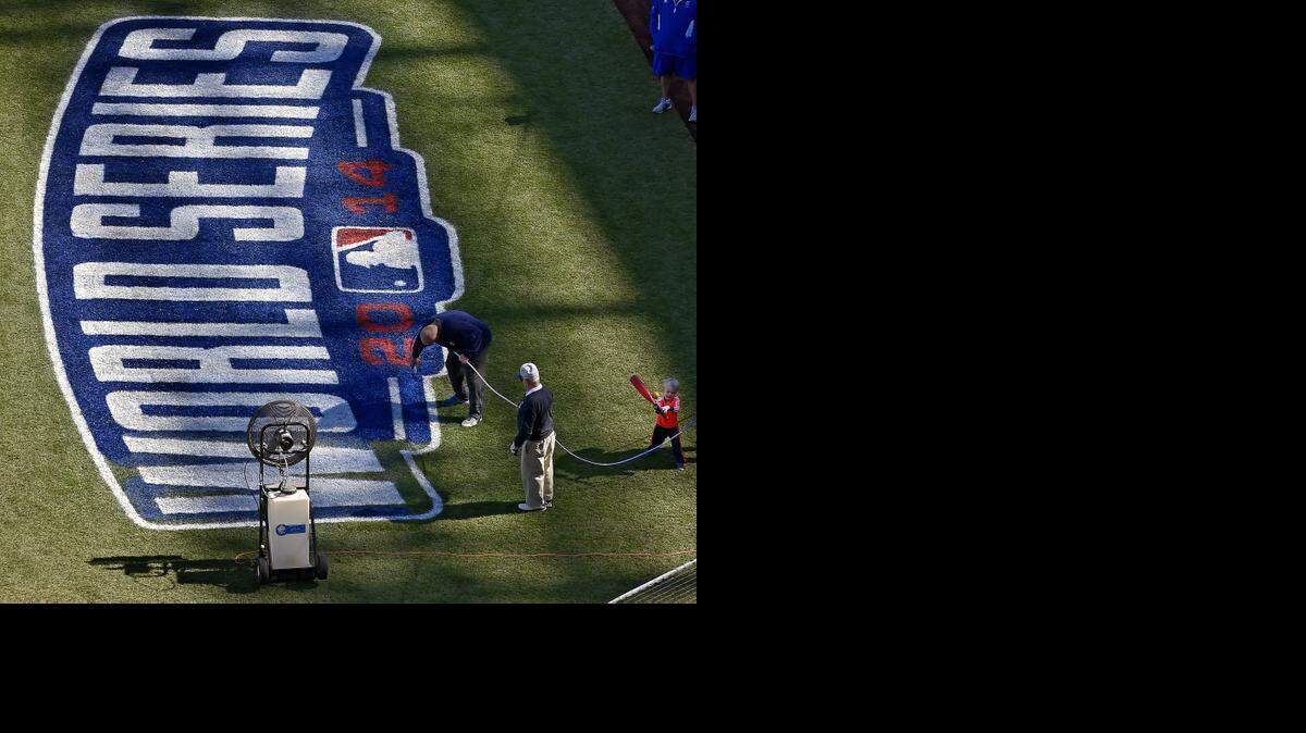 
George Toma watches as Scott Parker puts the finishing touchdown on the 2014 World Series logo as his son, Andrew, 3, plays with a ball and bat before Saturday's baseball practice for the Kansas City Royals on October 18, 2014 at Kauffman Stadium in Kansas City, Mo.
